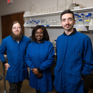 Three individuals wearing blue jackets in a scientific lab.